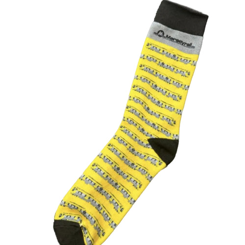 A single crew sock with a bright yellow body covered in horizontal Merseyrail 777 trains finished with a black cuff, heel, and toe. The brand name 'Merseyrail' is printed on the cuff.